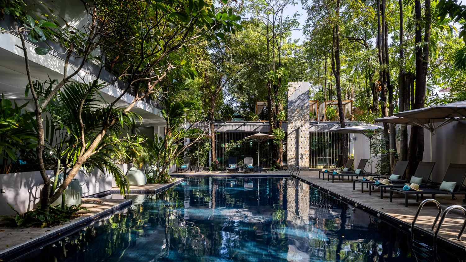 Anjali by Syphon serene outdoor swimming pool surrounded by lush greenery and modern architectural villas in Siem Reap under a clear sky.